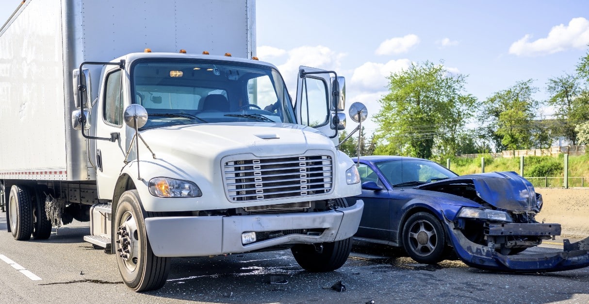 A large white commercial van is seen with heavy front-end damage after colliding with a smaller vehicle.
