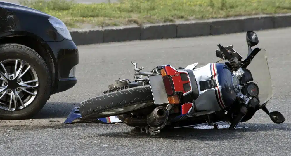 A motorcycle lies on its side on the asphalt of a residential street. The image focuses on the immediate physical damage following the accident.